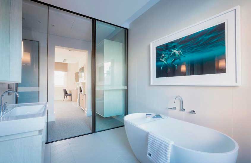 Banheiro de um hotel com banheira, pia, quadro decorativo equarto no fundo