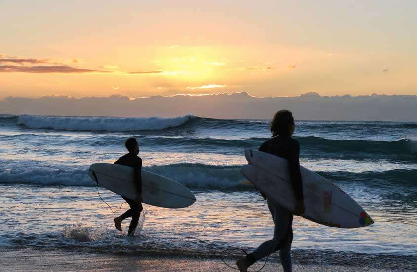 Durante o pôr do sol, pessoas passeando na praia com prancha de surf