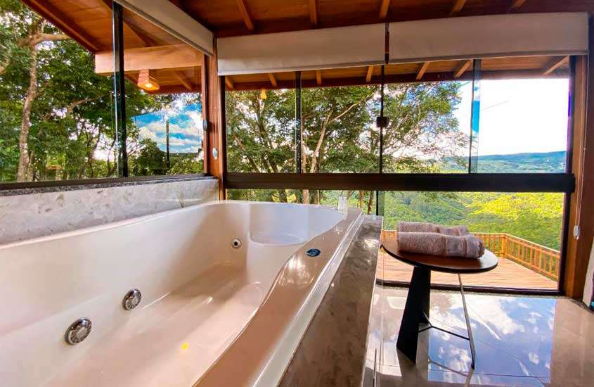 Área de banheira com toalhas, janelas grandes e paisagem da natureza