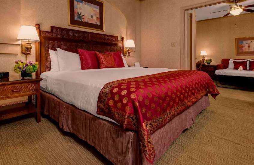 Quarto de hotel perto da Times Square com cama de casal, criado de madeira, quadros decorativos, vetilador de teto, sofá e decorações vermelhas