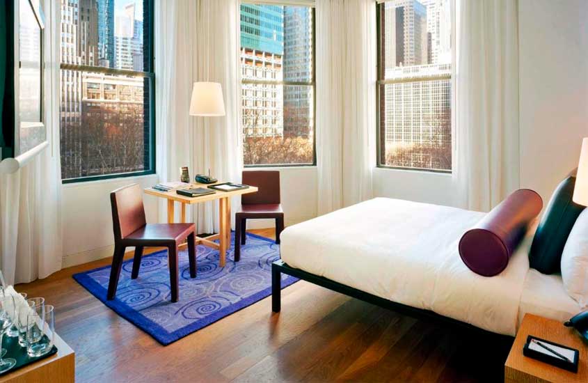 Quarto hotel perto da Times Square com cama, mesa, cadeiras, tapete e janelas acortinadas