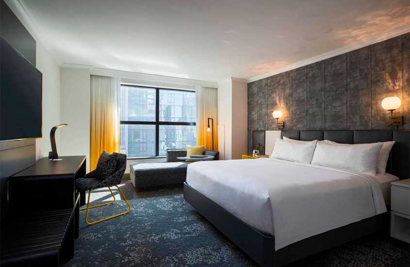 Quarto de um dos hotéis perto da Times Square com cama de casal, mesa de trabalho, sofás, janelas grandes acortinadas, criados e TV