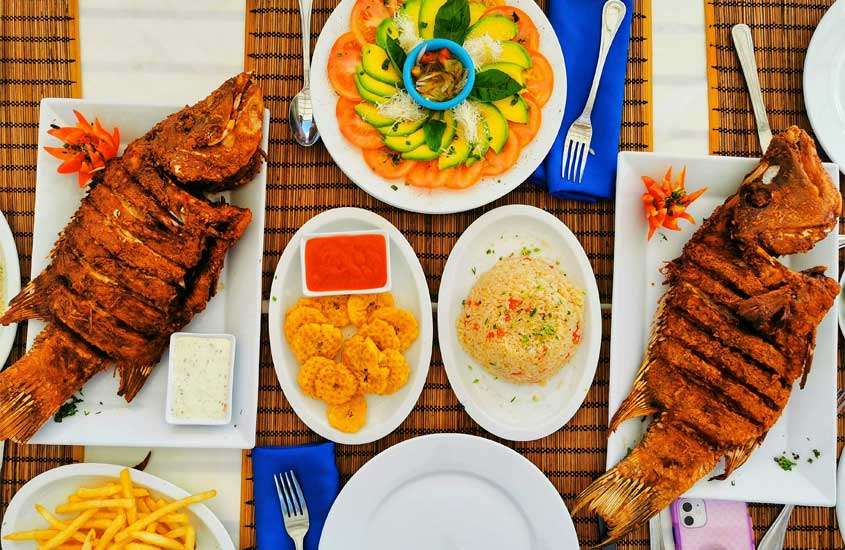 Mesa posta com peixe frito, saladas, arroz, batata frita, talheres e pratos