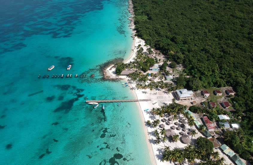 Visão aérea de Punta cana com praia de um lado com barcos e cidade do outro com natureza ao redor