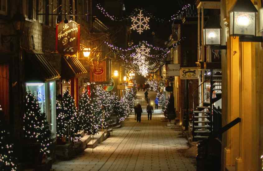 Durante a noite, rua iluminada com enfeites de natal e lojas coloridas