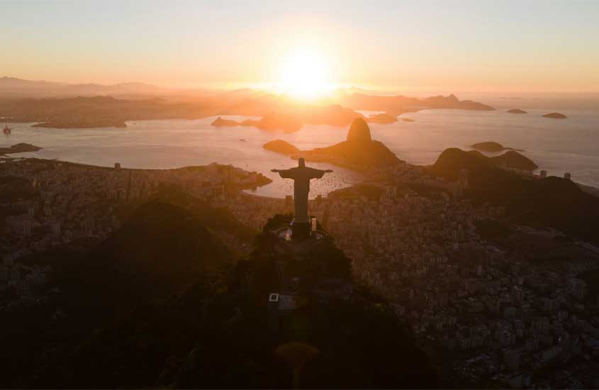 Durante o nascer do dia, vista aérea do Rio de Janeiro com Cristo Redentor no meio, cidade embaixo e praia na frente