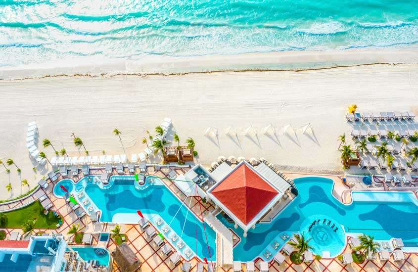Vista aérea da praia de Cancun com hotel atrás com piscinas, guarda-sóis, árvores e tendas ao redor