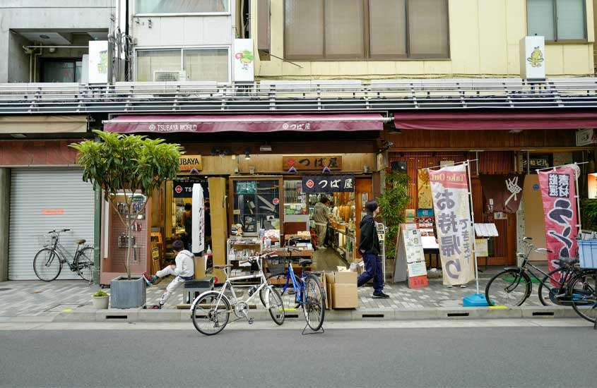 Durante o dia, rua de Asakusa com pessoas, bicicletas, árvores e lojinhas ao redor