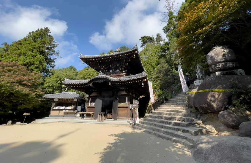 Em um dia de sol, templo na ilha de miyajima com árvores, pedras e escadaria ao redor