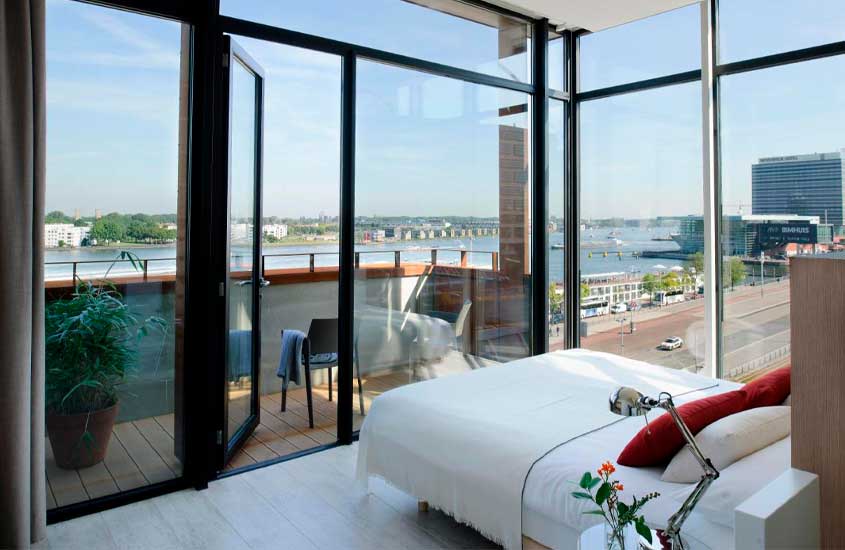 Quarto de um hotel com cama de casal, flor decorativa, varanda com paisagem da cidade e do mar