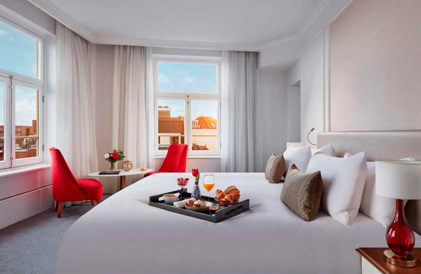 Interior de quarto de hotel em amsterdã com cama de casal, poltronas, mesa, bandeja de café da manha e janelas grandes acortinadas