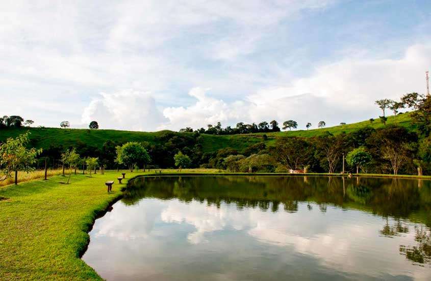 Em um dia de sol com nuvens, lago de hotel fazenda perto de poços de caldas com bancos, árvores e plantas ao redor