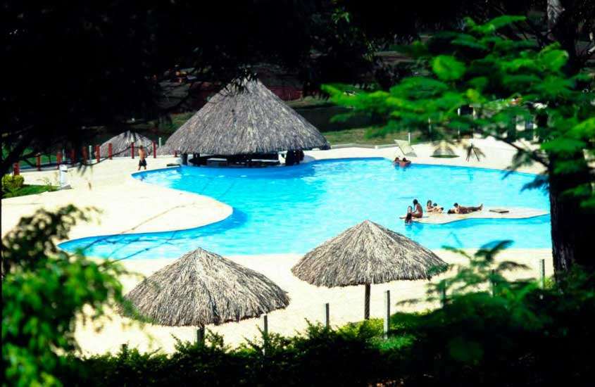 Área de lazer de hotel fazenda perto de poços de caldas com piscina, tendas de palha e árvores ao redor