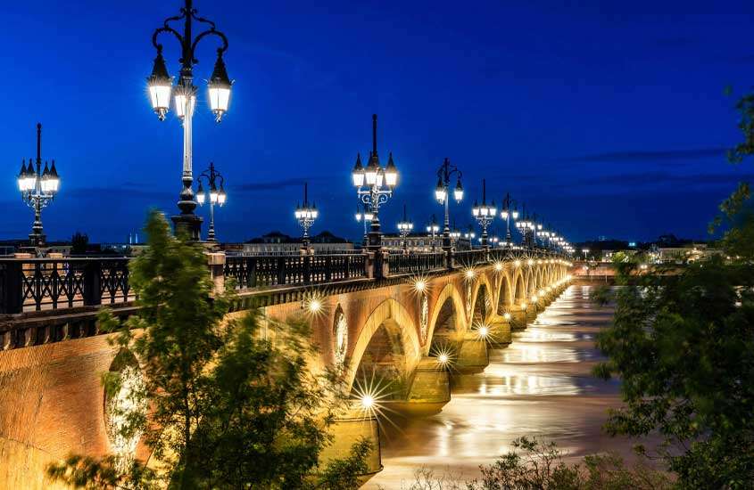 Durante o anoitecer, ponte famosa de bordeaux com luzes iluminando e árvores ao redor