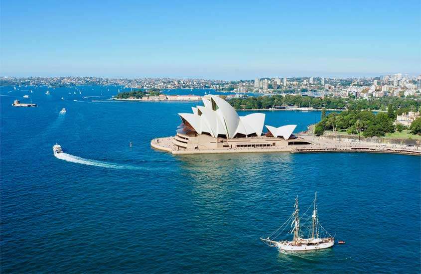 Em um dia ensolarado, visão aérea de um dos pontos turísticos de Sydney com mar, cidade e barcos ao redor