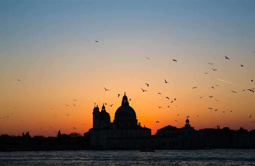 Durante o pôr do sol paisagem da cidade de Veneza com canal na frente e pássaros ao redor