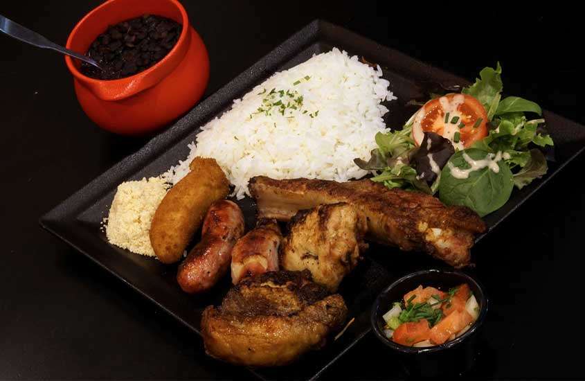 Prato de comida brasileira com churrasco, arroz, farofa, salada e feijão
