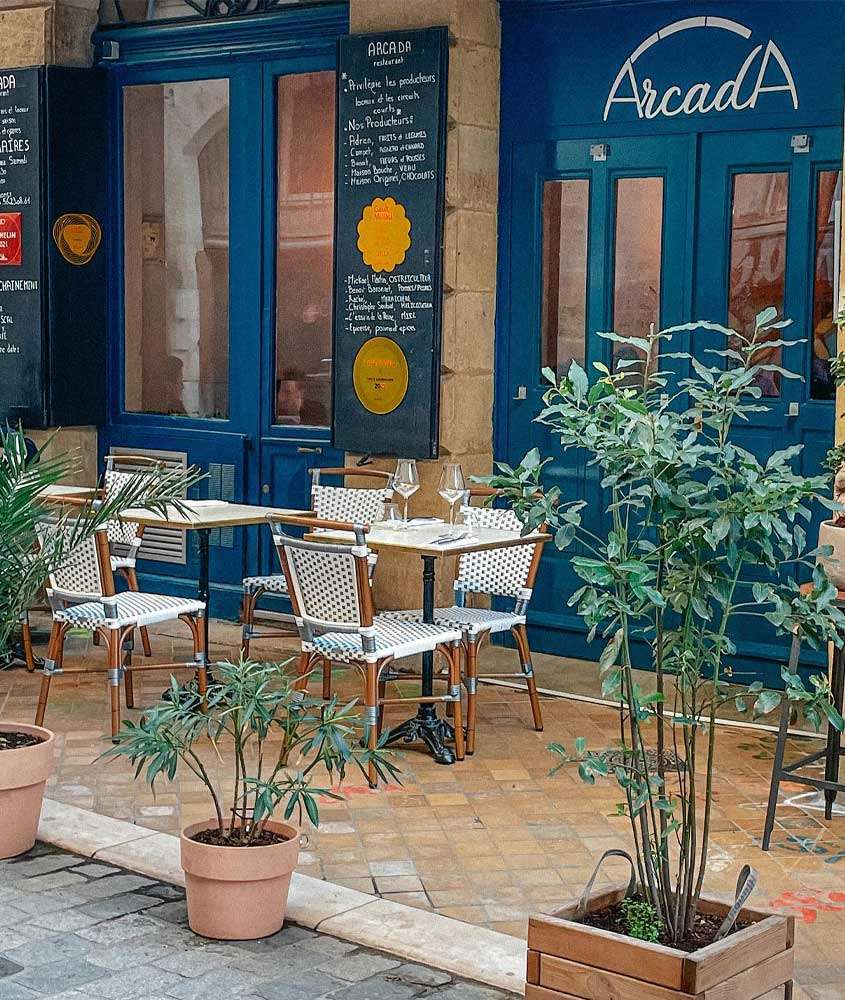 Fachada de um dos restaurantes em Bordeaux com mesas, cadeiras, portas grandes e plantas ao redor