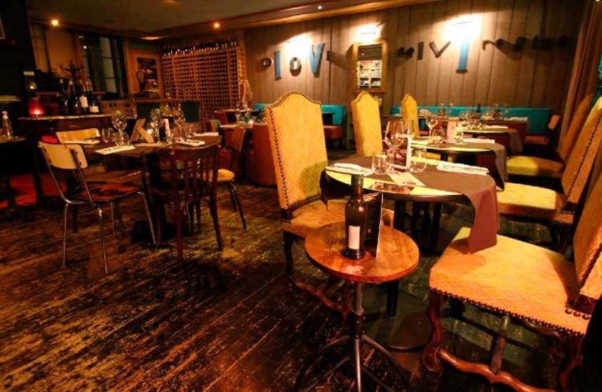 Interior de restaurante com mesas, cadeiras, vinho e bar do lado