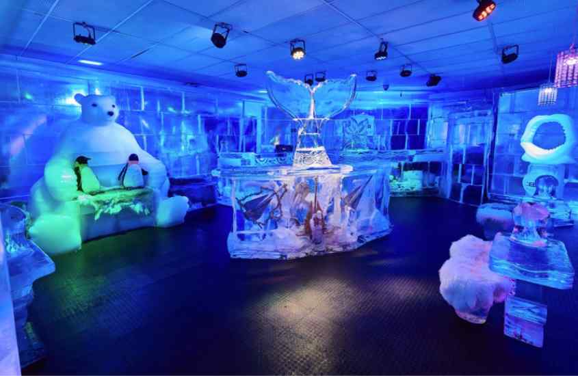 Interior do ICEBAR com esculturas de gelo, mesas, cadeiras, urso polar e pinguins decorativos