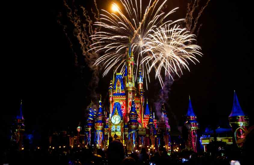Durante a noite de Réveillon em Orlando, castelo da Disney iluminado por fogos de artifício e luzes coloridades com pessoas ao redor
