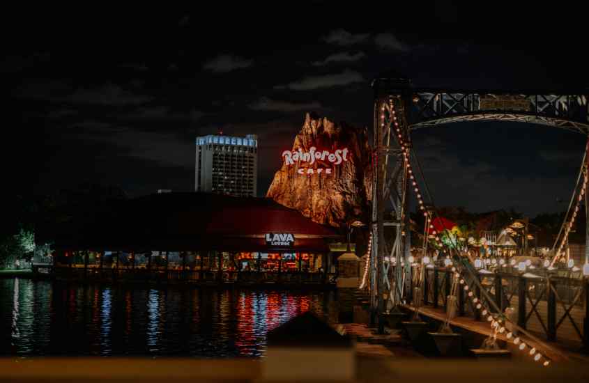 Durante a noite, ponte iluminada da Disney springs com lago embaixo, restaurantes e lojas ao redor, um lugar super legal para comemorar o Réveillon em Orlando