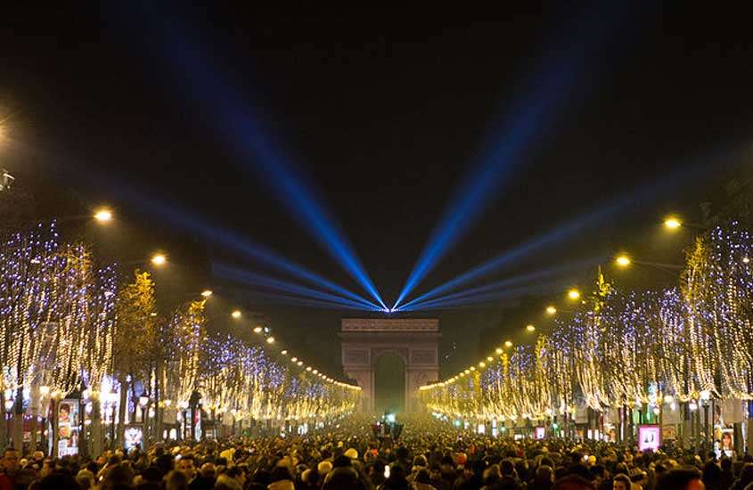 Durante a noite de Réveillon em Paris pessoas de frente a um ponto turístico com luzes iluminando as árvores
