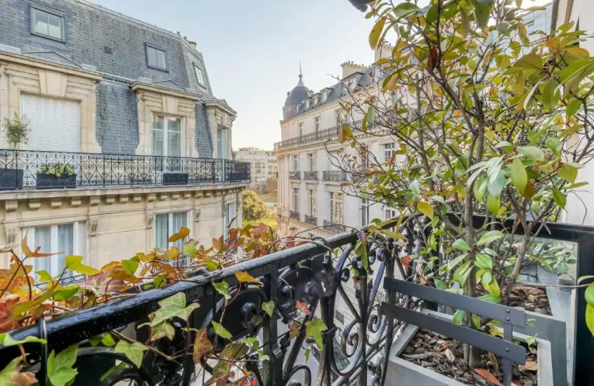 Varanda acolhedora com vista para charmosos edifícios históricos em Paris, rodeada de plantas que adicionam um toque de natureza ao ambiente urbano.