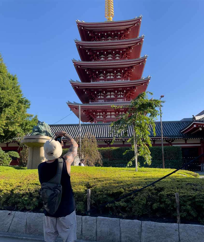 Em um dia ensolarado, Vagner tirando foto do pagode do templo senso-ji com plantas e árvores ao redor