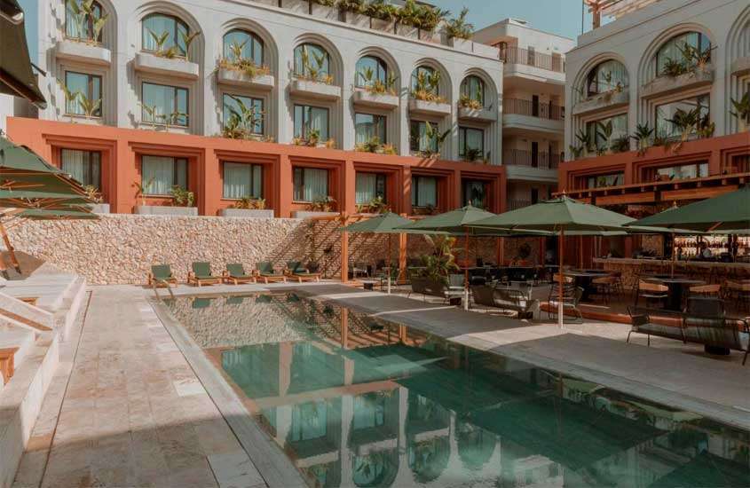 Em um dia de sol, área de lazer de um hotel para passar o Réveillon em Cartagena das Índias, com piscina, espreguiçadeiras, mesas, cadeiras, guarda-sóis e plantas decorativas ao redor