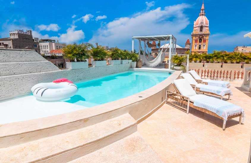 Em um dia ensolarado, área de lazer de um hotel para passar o Réveillon em Cartagena das Índias, com piscina, espreguiçadeiras, redes e paisagem da cidade