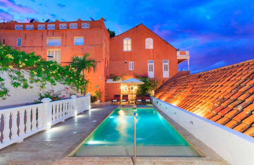 Durante o anoitecer, área de lazer de um hotel para passar o Réveillon em Cartagena das Índias, com piscina, espreguiçadeiras, guarda-sol e plantas ao redor