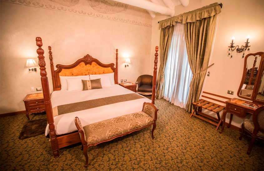 Quarto de um hotel para passar o Réveillon em Cusco 2024/2025, com cama de casal, poltrona, janela grande acortinada e móveis de madeira