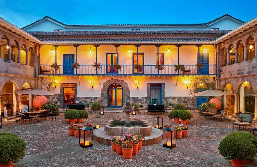 Durante o anoitecer, área externa de um hotel para passar o Réveillon em Cusco com plantas, árvores, mesas, cadeiras, velas e guarda-sóis ao redor