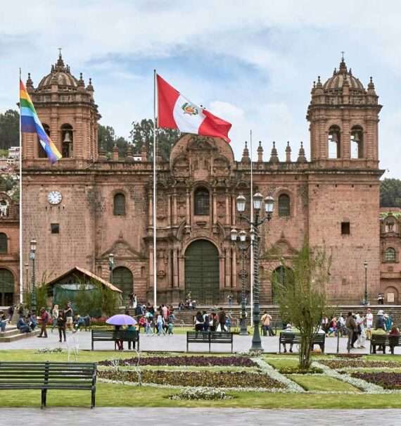 Durante a tarde, fachada de um dos pontos turísticos em Cusco com árvores e pessoas ao redor