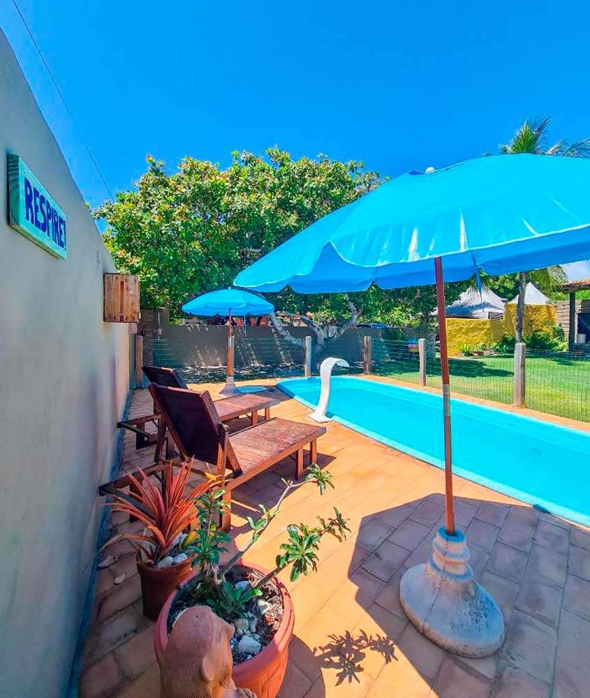 Em um dia de sol, área de lazer de um dos hotéis fazenda em Alagoas com piscina, espreguiçadeiras de madeira, guarda-sóis e plantas ao redor