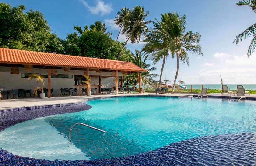 Em um dia de sol, área de lazer de um hotel fazenda em Alagoas com piscina, espreguiçadeiras, mesas, cadeiras e plantas