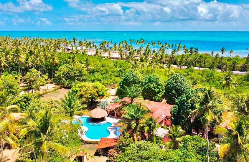 Em um dia ensolarado, visão aérea de um dos hotéis fazenda em Alagoas com piscina, árvores, plantas e praia do lado