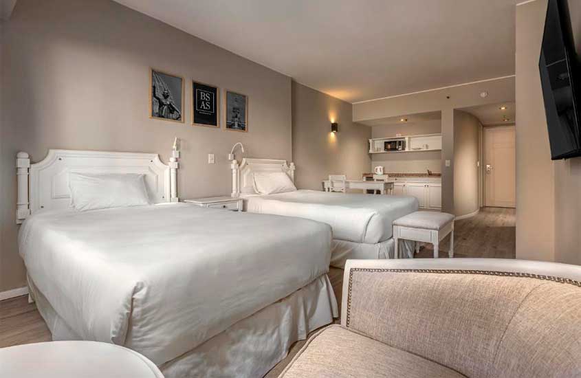 Quarto luxuoso de um dos hotéis em Buenos Aires para brasileiros com camas grandes, poltronas, TV, quadros decorativos, cozinha cinpacta, mesa e cadeiras