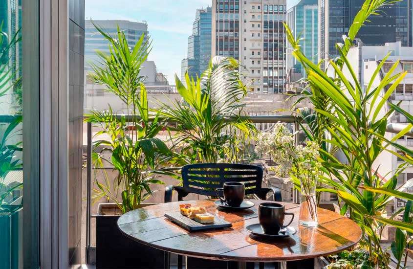 Em um dia de sol, varanda de um dos hotéis em Buenos Aires para brasileiros com mesa, cadeiras, café da manhã e plantas decorativas