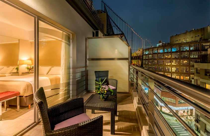 Durante a noite, varanda do quarto de um dos melhores hotéis em Buenos Aires para brasileiros com mesas, cadeiras, plantas decorativas e paisagem da cidade