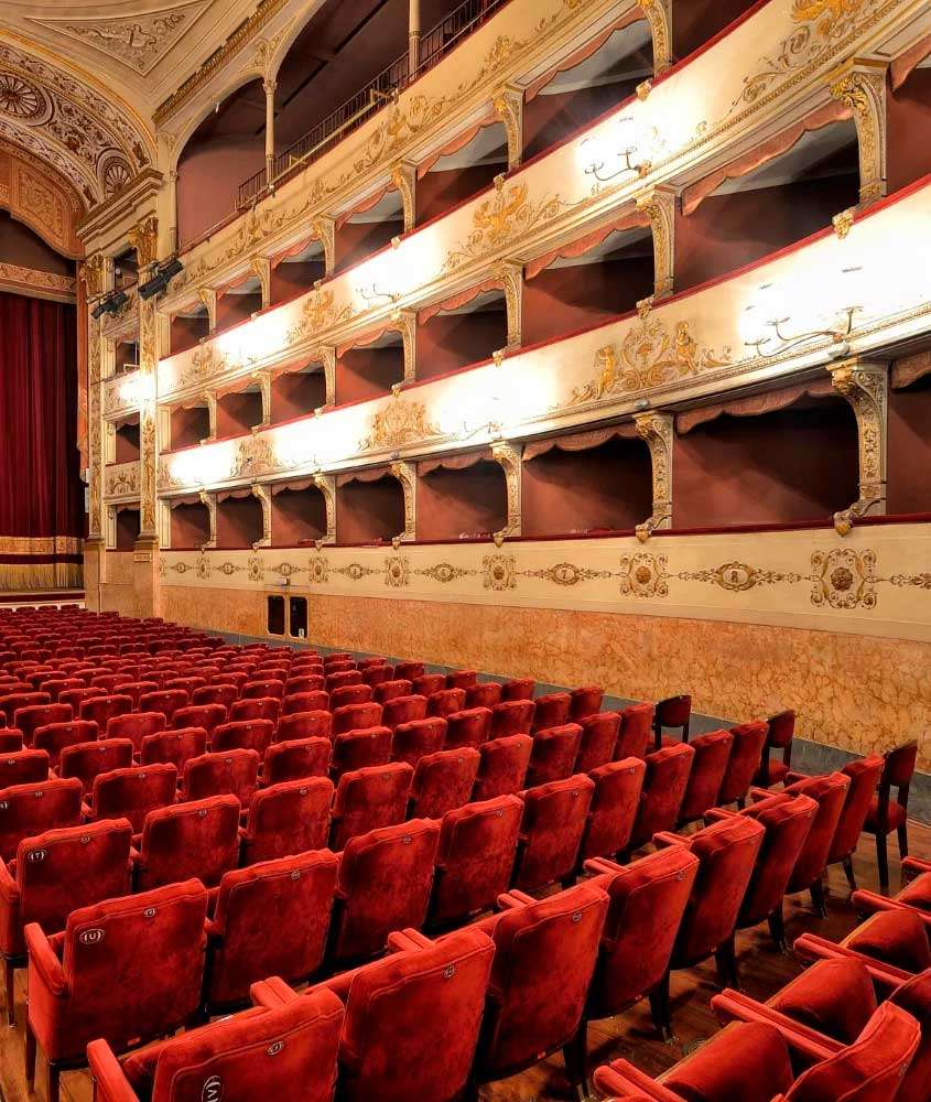 Interior do Teatro della Pergola com paredes ornamentadas e cadeiras de veludo vermelho