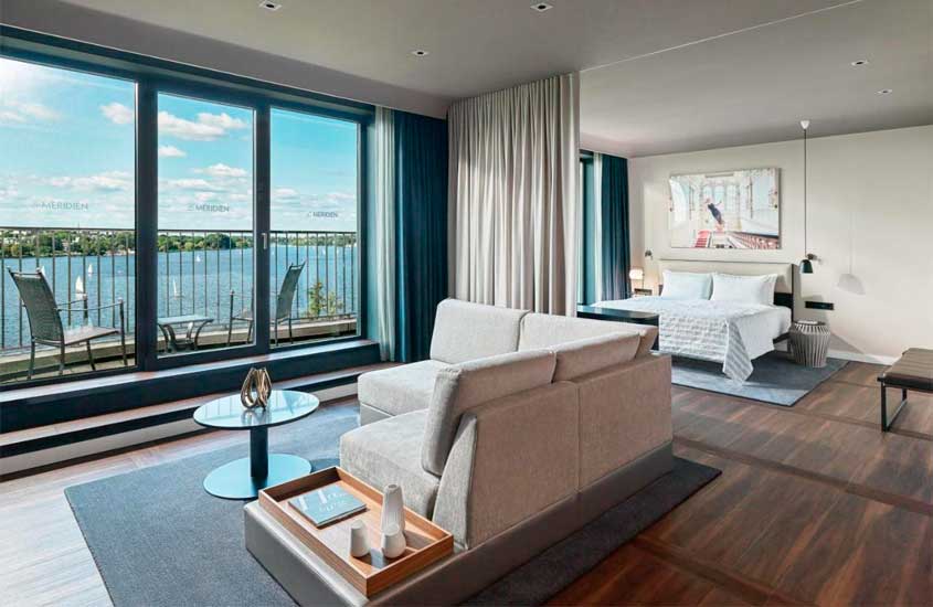 Quarto de hotel em Hamburgo com cama de casal, varanda, mesas, cadeiras, sofá, quadro decorativo e paisagem da cidade