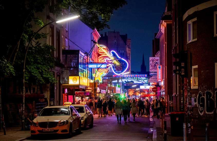 Durante a noite, bairro de St. Pauli iluminado com luzes coloridas, carros, pessoas e prédios ao redor