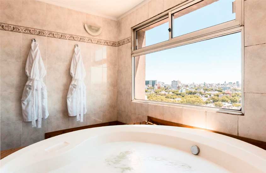 Banheira de um hotel para passar o réveillon em Montevidéu com deck de madeira, roupões e janela com vista