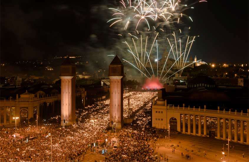 Durante a noite Plaça Espanya comemorando a virada de ano com a queima de fogos, pessoas ao redor e prédios históricos