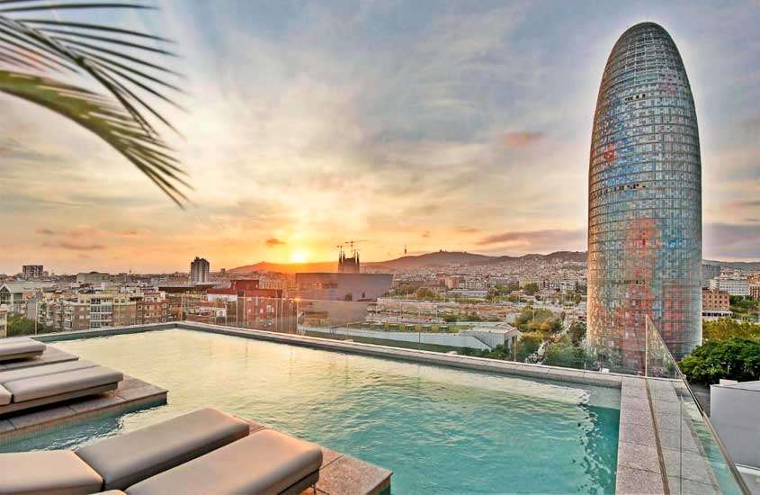Em um final de dia, cobertura de um hotel para passar o ano novo em Barcelona com piscina, espreguiçadeiras e paisagem da cidade