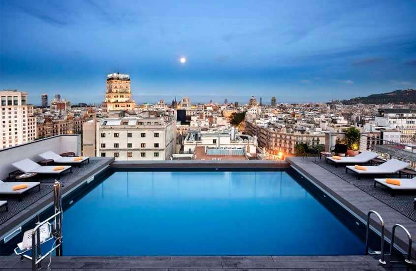 Durante a manhã, cobertura de um hotel para passar o Réveillon em Barcelona com piscina, espreguiçadeiras e paisagem da cidade