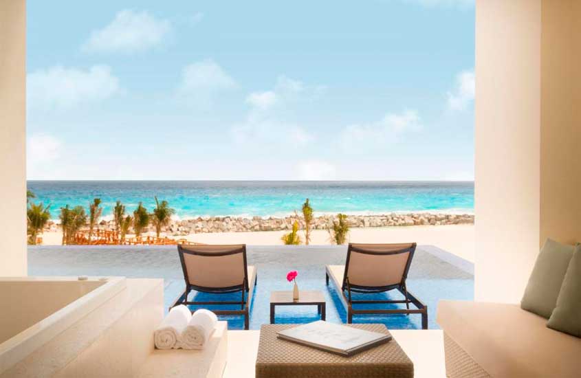 Em um dia de sol, área de lazer de um hotel para passar o ano novo em Cancún com piscina de borda infinita, espreguiçadeiras, sofás, banheira e pria na frente
