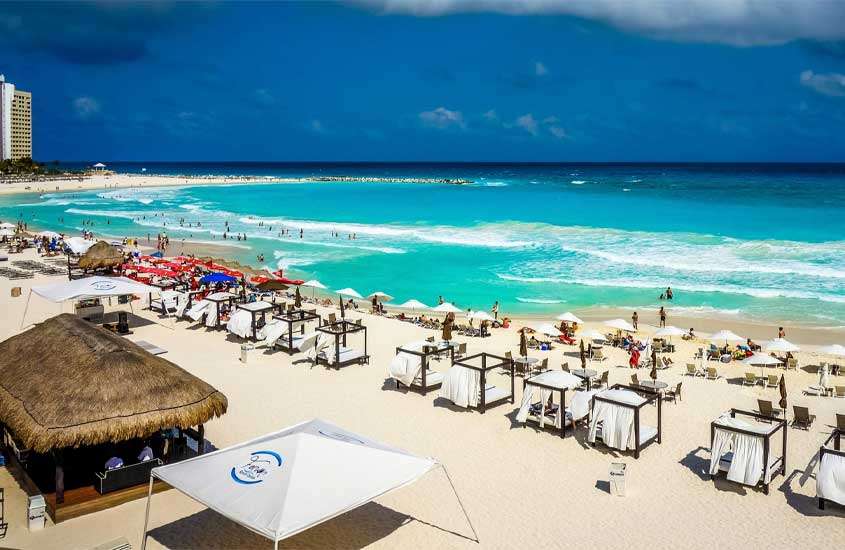 Em um dia ensolarado, Playa Forum para passar o Réveillon em Cancún com tendas, guarda-sóis, mesas, cadeiras e pessoas ao redor